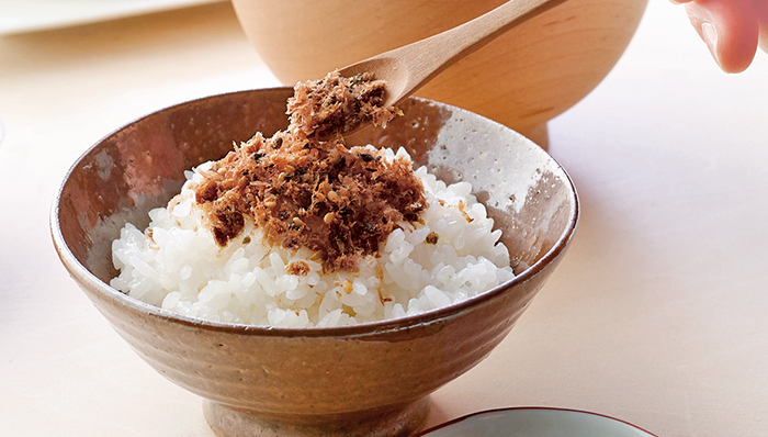 ごはんの上にかつおのふりかけがかかり、スプーンでそのふりかけを持ち上げている