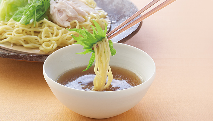 白い器に入ったスープにちぢれ麺をつけている写真